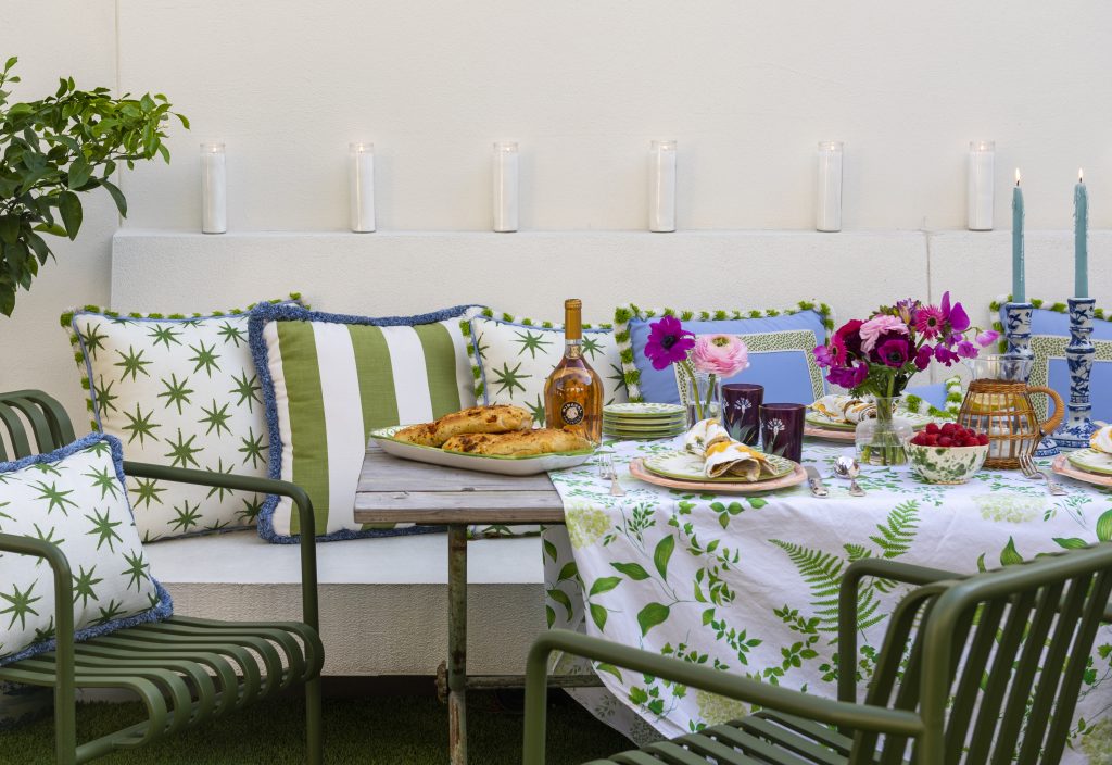 Outdoor dining area with banquette and table set with flowers and tablecloth in blues, greens, and pinks